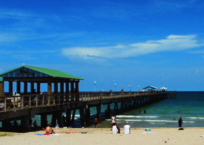 Photo of the pier off into the water with people on the pier and beach.